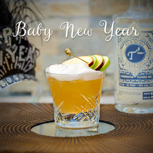 Cocktail with apple garnish and bottle of vodka on a table, text 'Baby New Year' above.