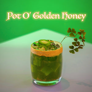 Green cocktail in a glass with garnishes on a white surface, featuring 'Pot O' Golden Honey' text.